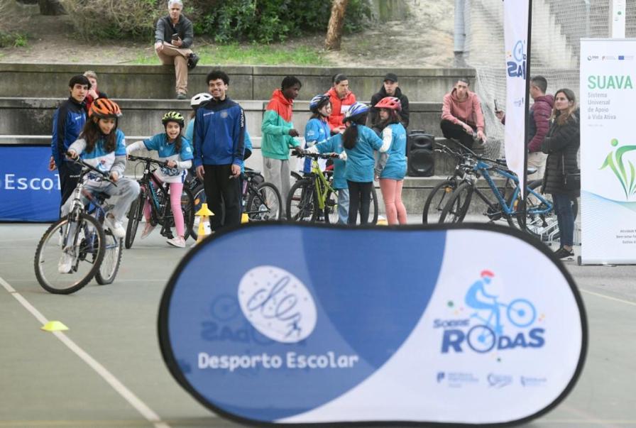 Alunos com bicicletas e placa do Desporto Escolar sobre rodas